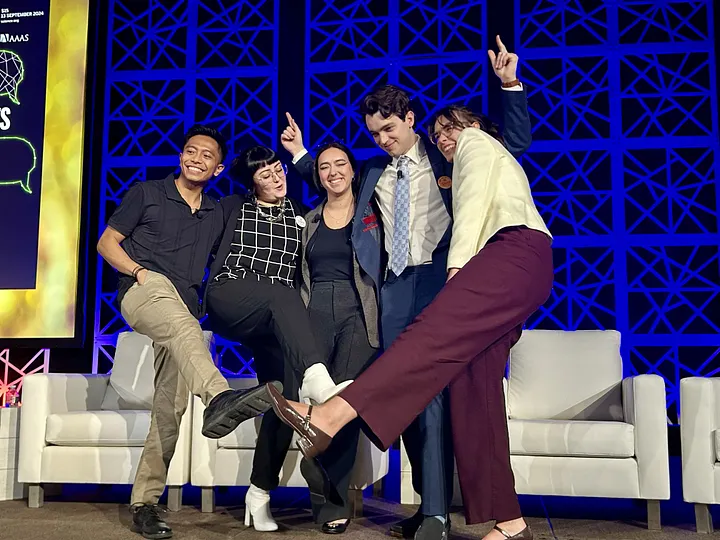 A group of founding SNAP members pose for a silly photo with legs out and arms up after the end of the first AAAS plenary discussion featuring ECRs.