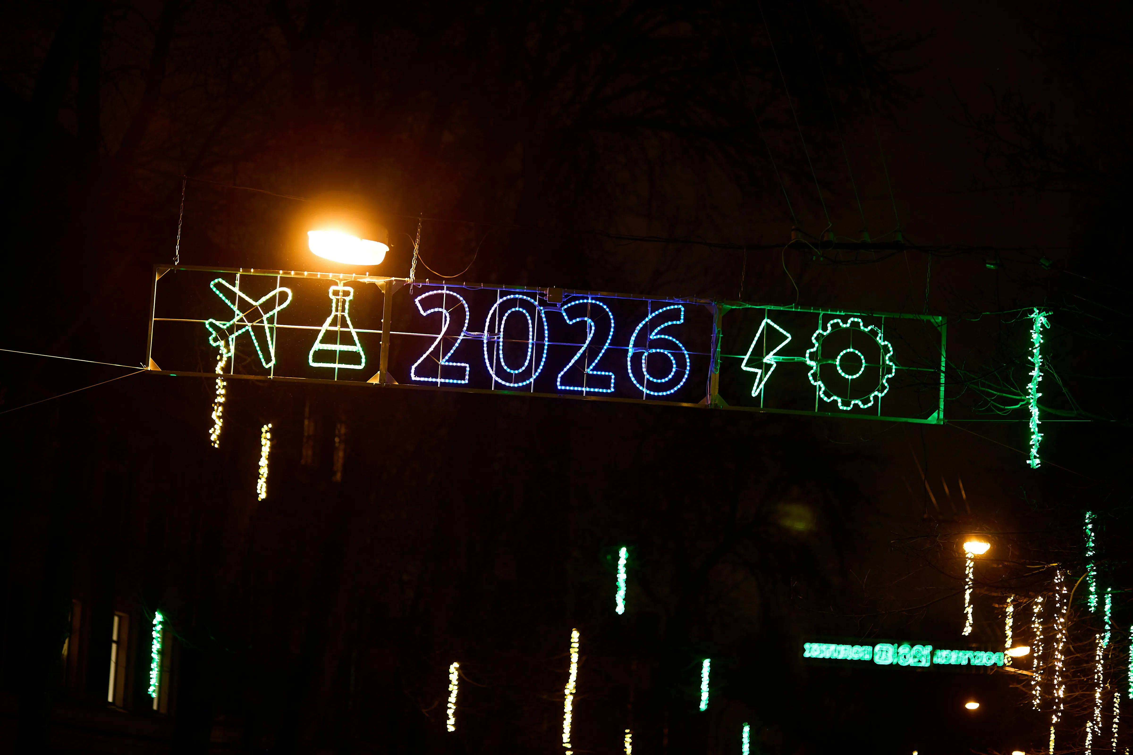 Neon light display showing a plane, flask, the year 2026, a lightning bolt, and a gear against a dark night sky