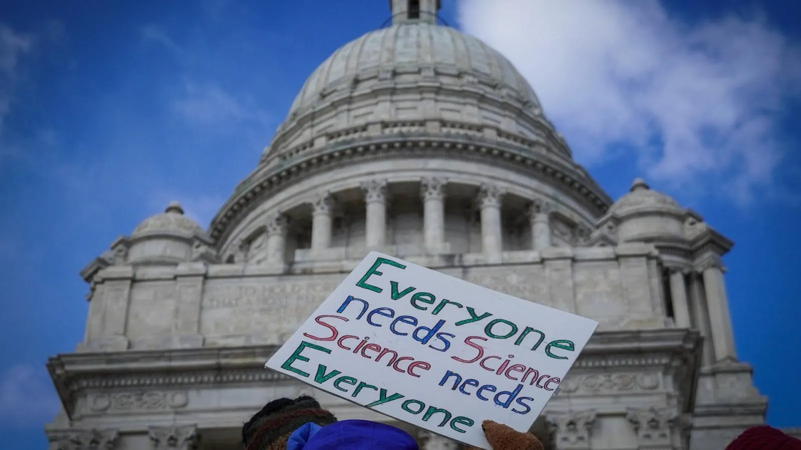 A demonstrator holds a sign outside the Rhode Island State House during a rally against federal cuts to research funding, Providence, March 2025.