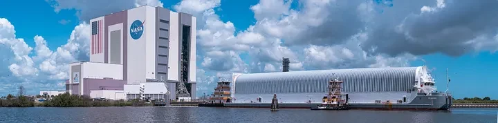 Roman's covered transport container aboard a barge docked beside the NASA Vehicle Assembly Building