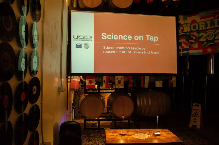 A projector screen reading Science on Tap above wine barrels and a wall of vinyl records at the brewery