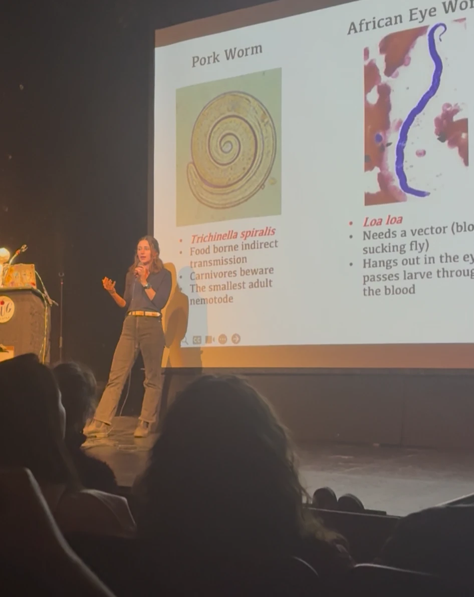 Emily Selland speaking at Nerd Nite Denver in front of a slide about parasitic worms