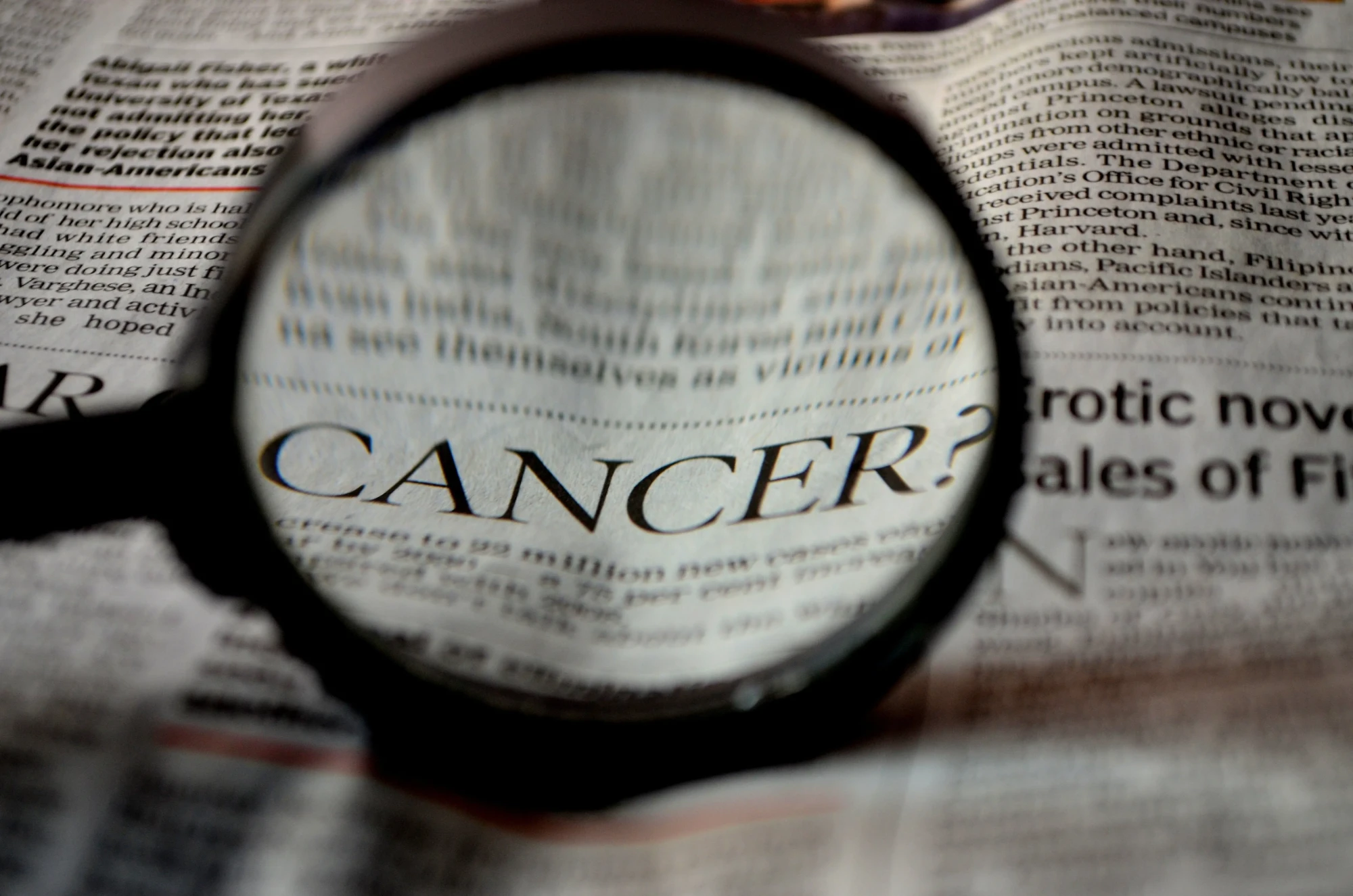 A magnifying glass over a newspaper, enlarging the word "CANCER?"