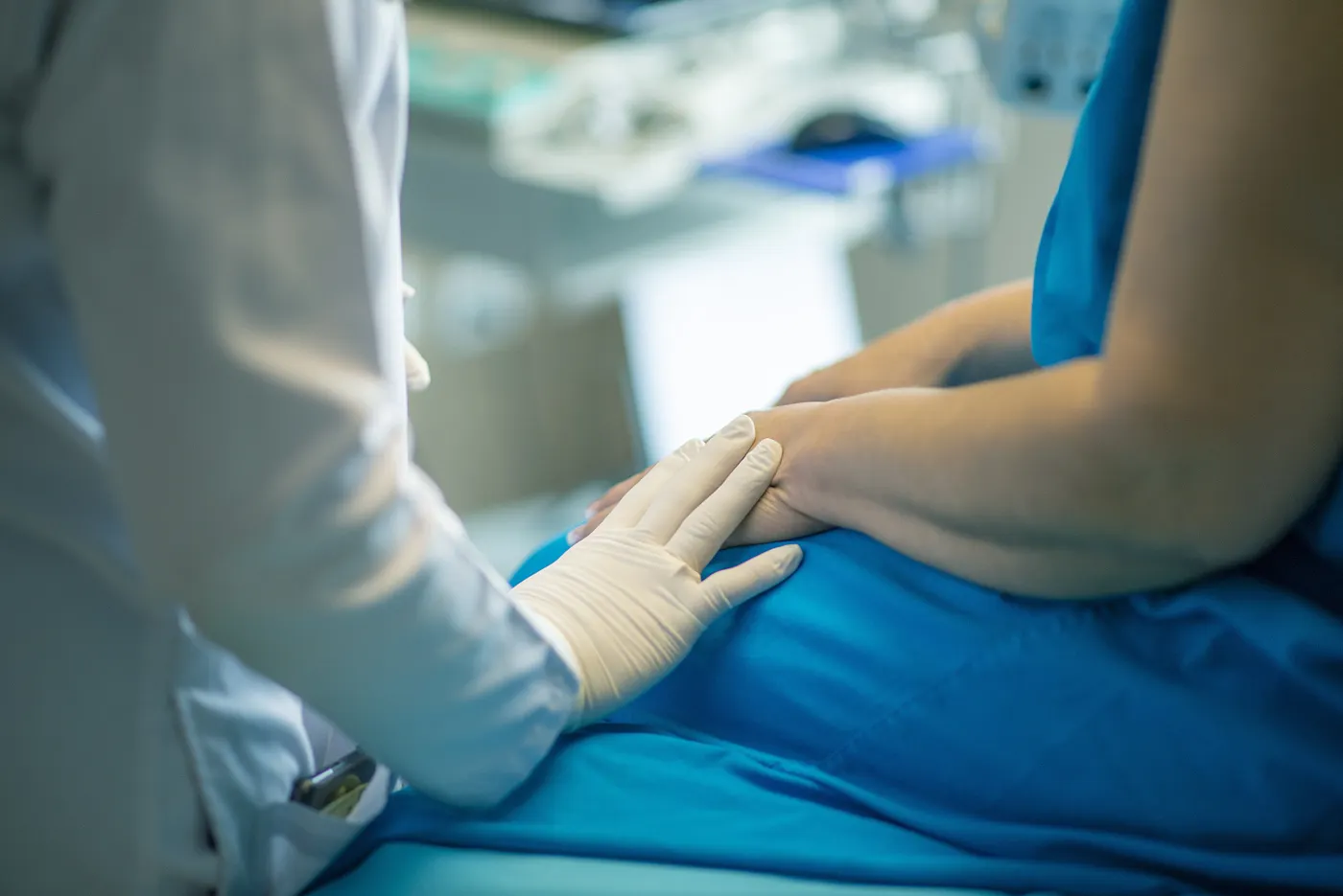 A clinician in gloves resting a hand on a patient's hands